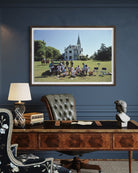 Framed picture of a group of people on a lawn with a large house in the background, displayed above a wooden desk.