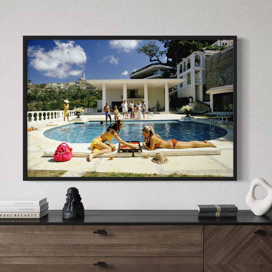 Mounted on a wall displaying an image of people by a pool, with decorative items on a wooden console table below.