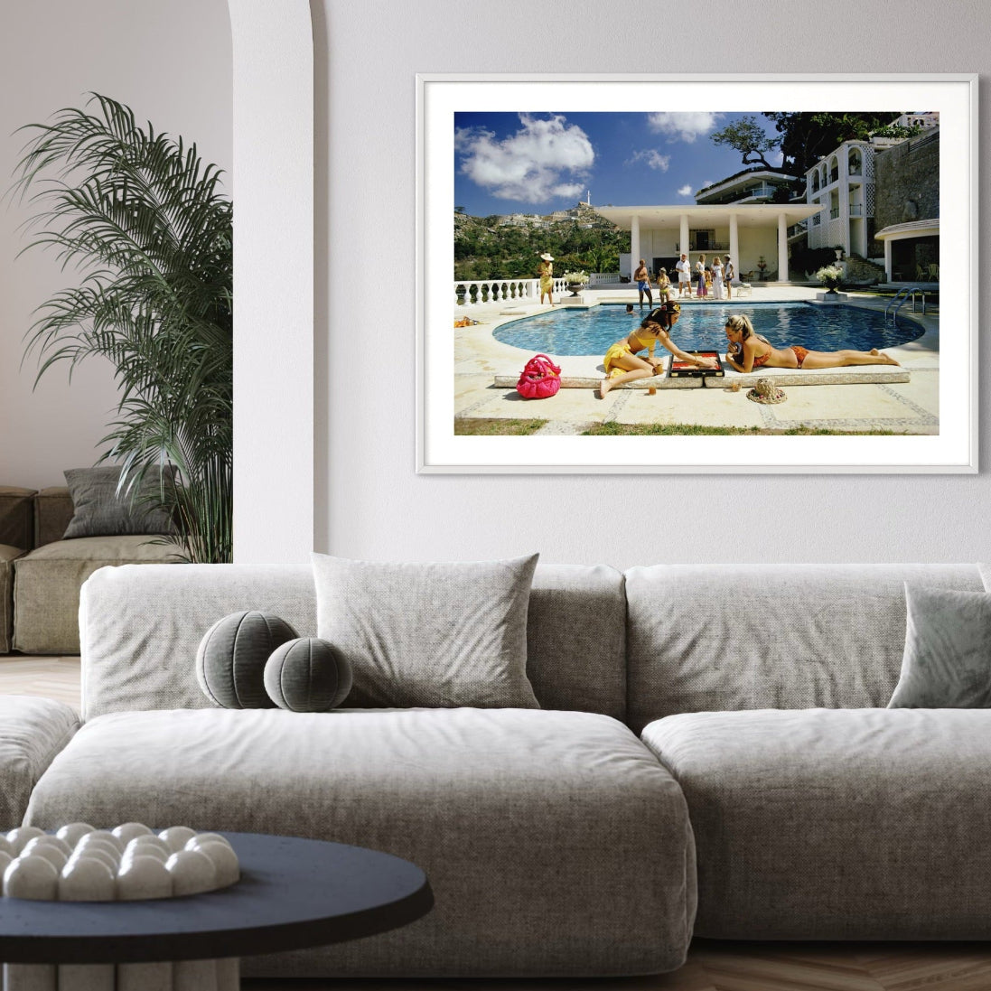 Framed photograph of people by a pool on a wall above a modern living room.