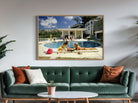 Framed artwork of people by a pool on a wall above a green sofa with decorative pillows.