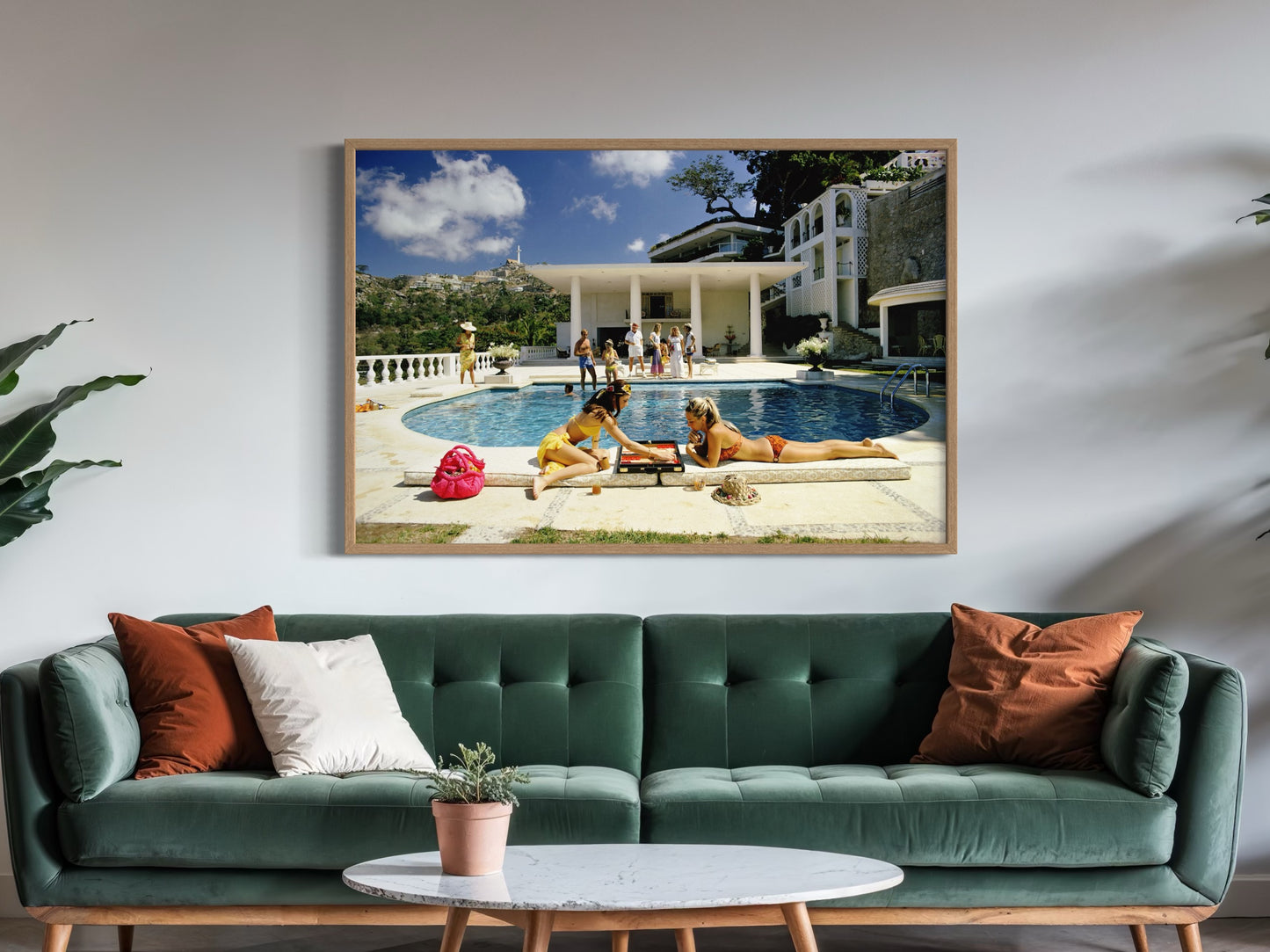 Framed artwork of people by a pool on a wall above a green sofa with decorative pillows.