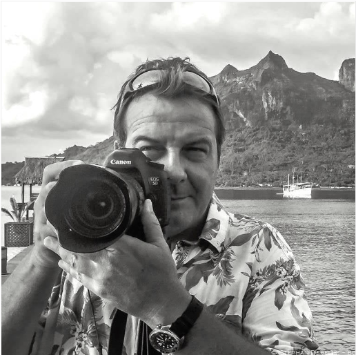 Person holding a Canon camera with a scenic background of mountains and water.
