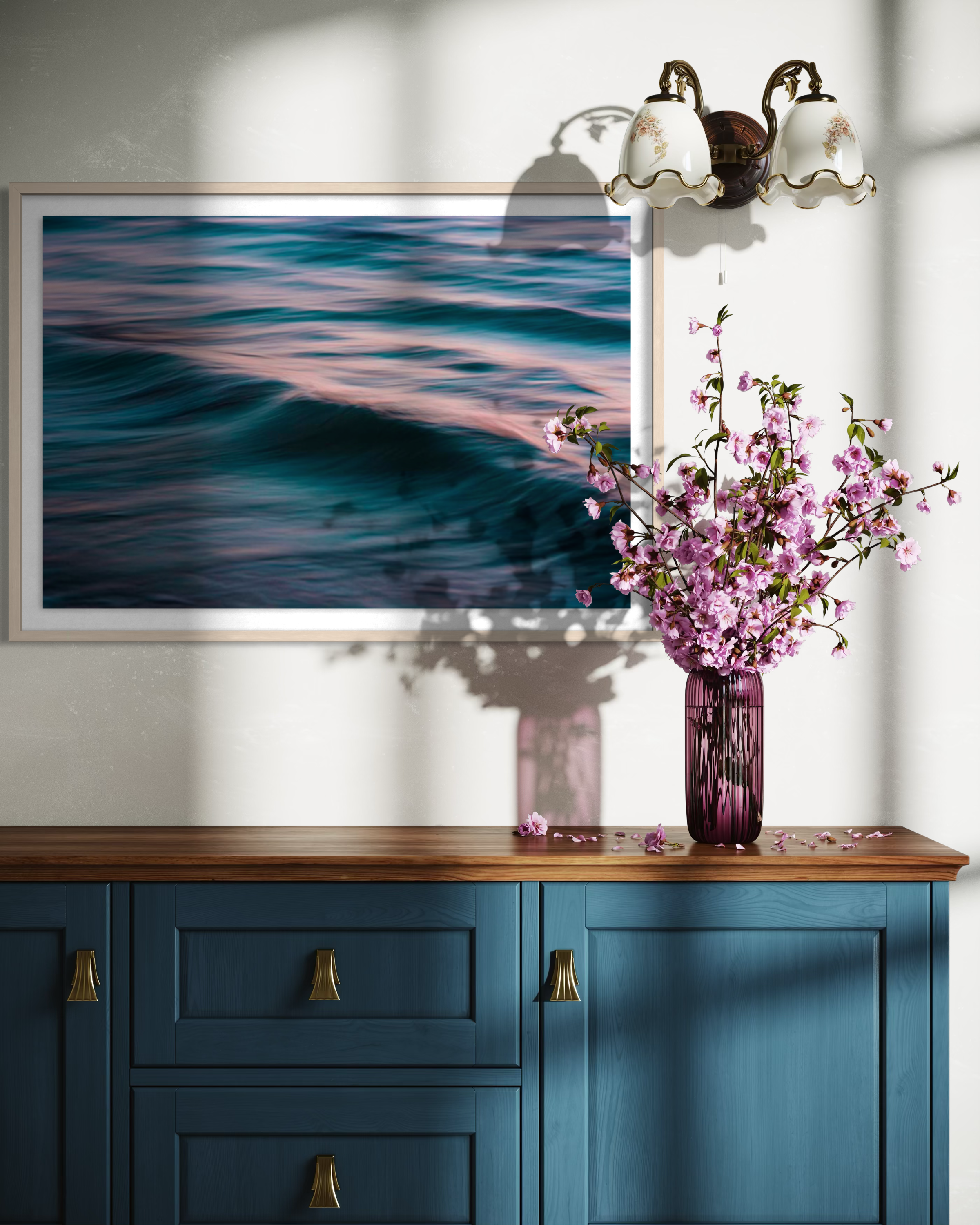 Blue cabinet with a wooden top, framed artwork of water, and a vase with pink flowers.
