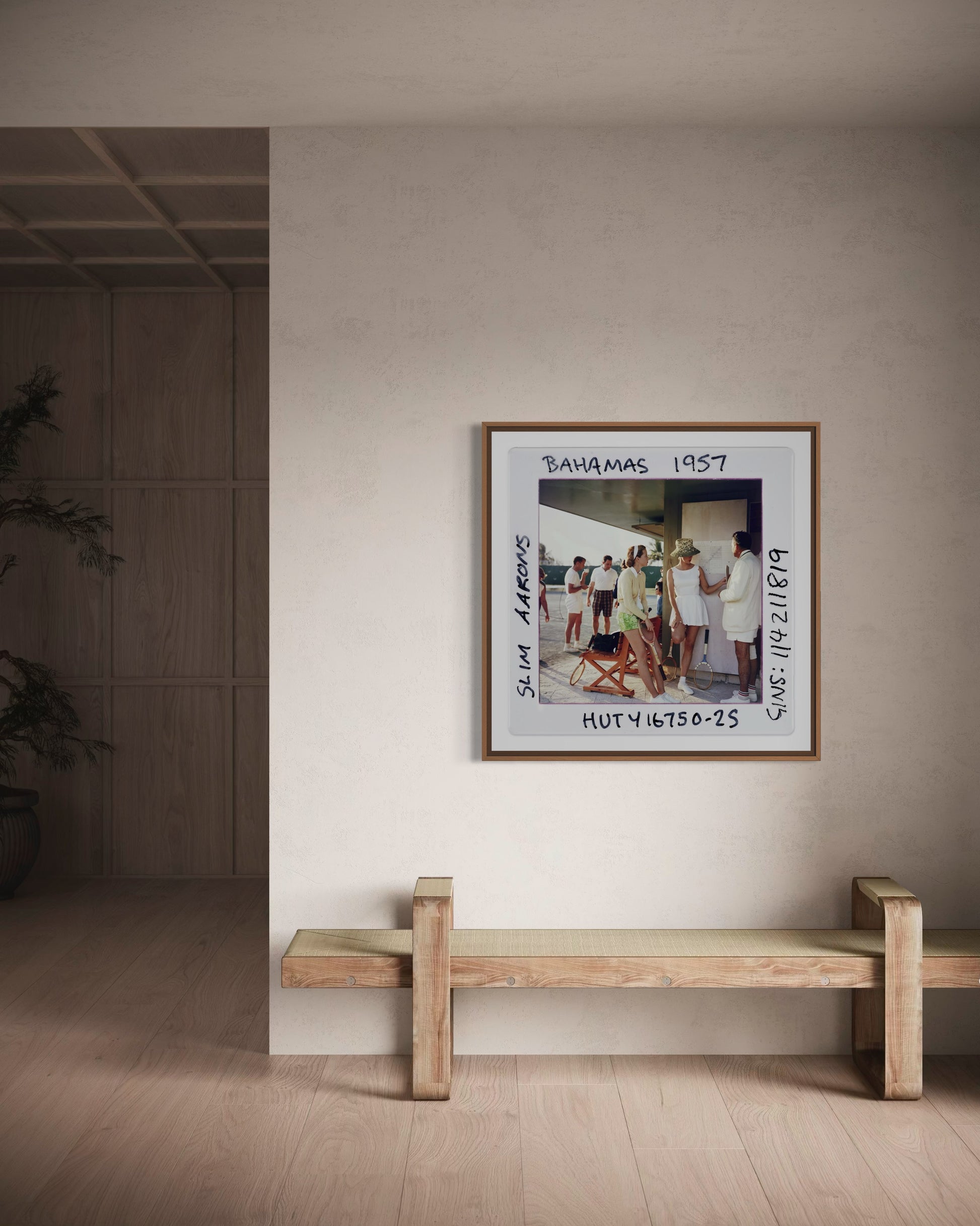 Framed artwork on a wall above a wooden bench in a minimalistic room.