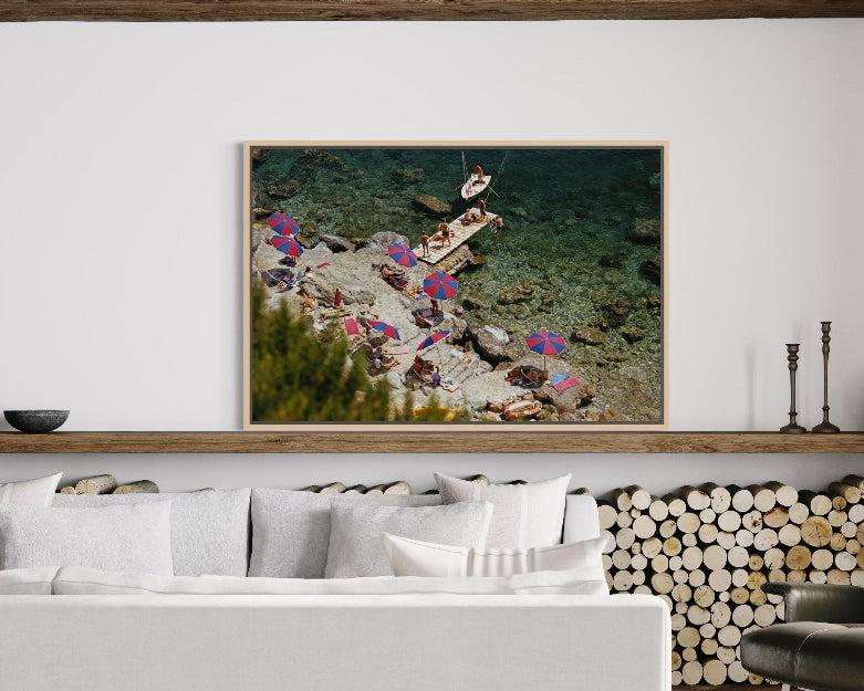 Framed artwork of people on a beach with a white wall and sofa in the background