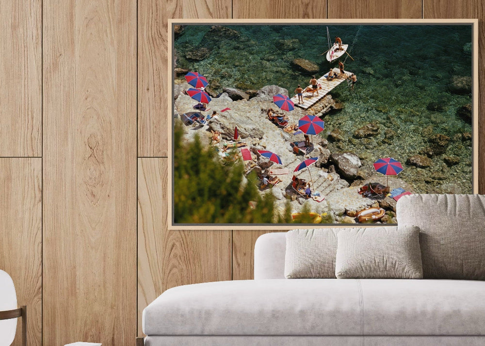 Framed artwork of a beach scene with people and umbrellas on a wooden wall above a sofa.