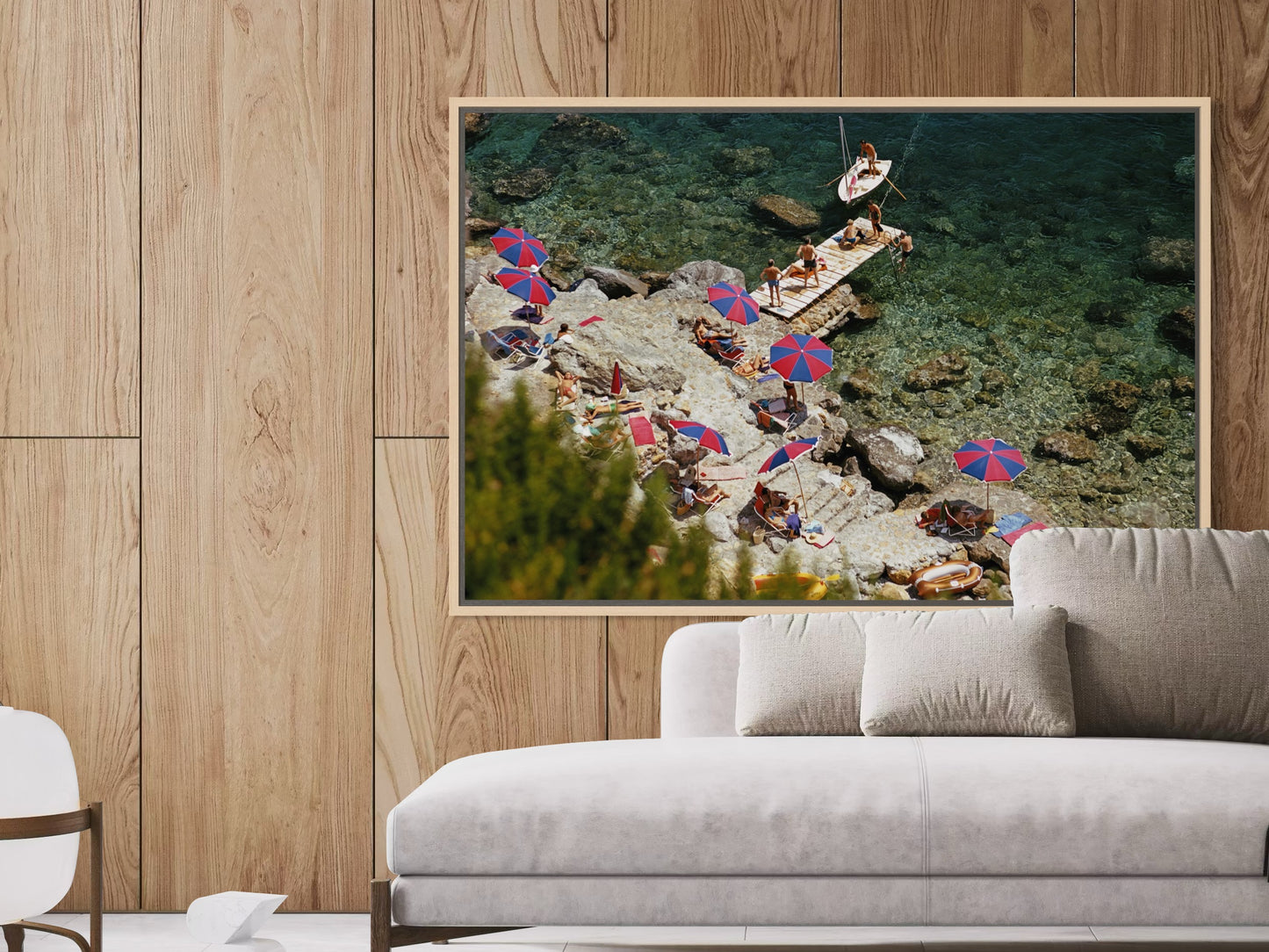 Framed artwork of a beach scene with people and umbrellas on a wooden wall above a sofa.