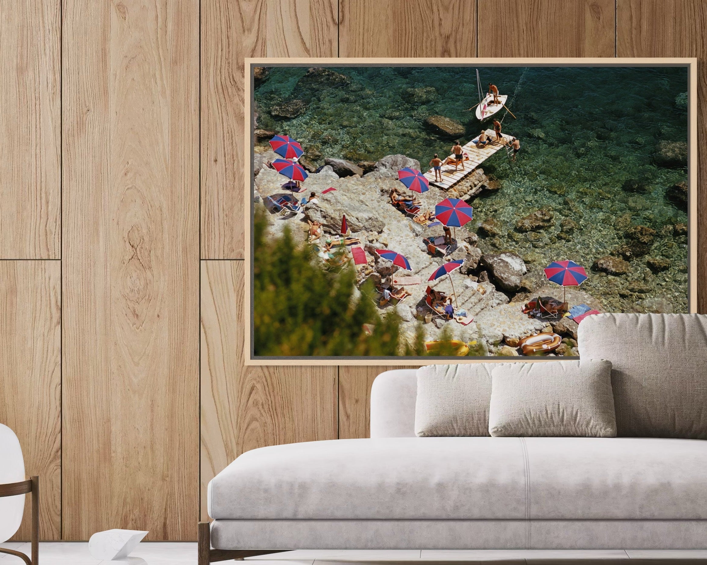 Framed artwork of a beach scene with people and umbrellas on a wooden wall above a sofa.