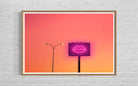Framed artwork of a neon sign with lips against an orange and pink gradient sky.