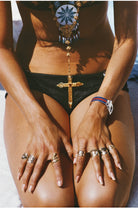 Person wearing a black swimsuit with decorative elements, sitting on a sandy surface. The Picturalist Wall Art and Photography for Designed Interiors. Slim Aarons Collection, Summer. Getty Images Gallery. 