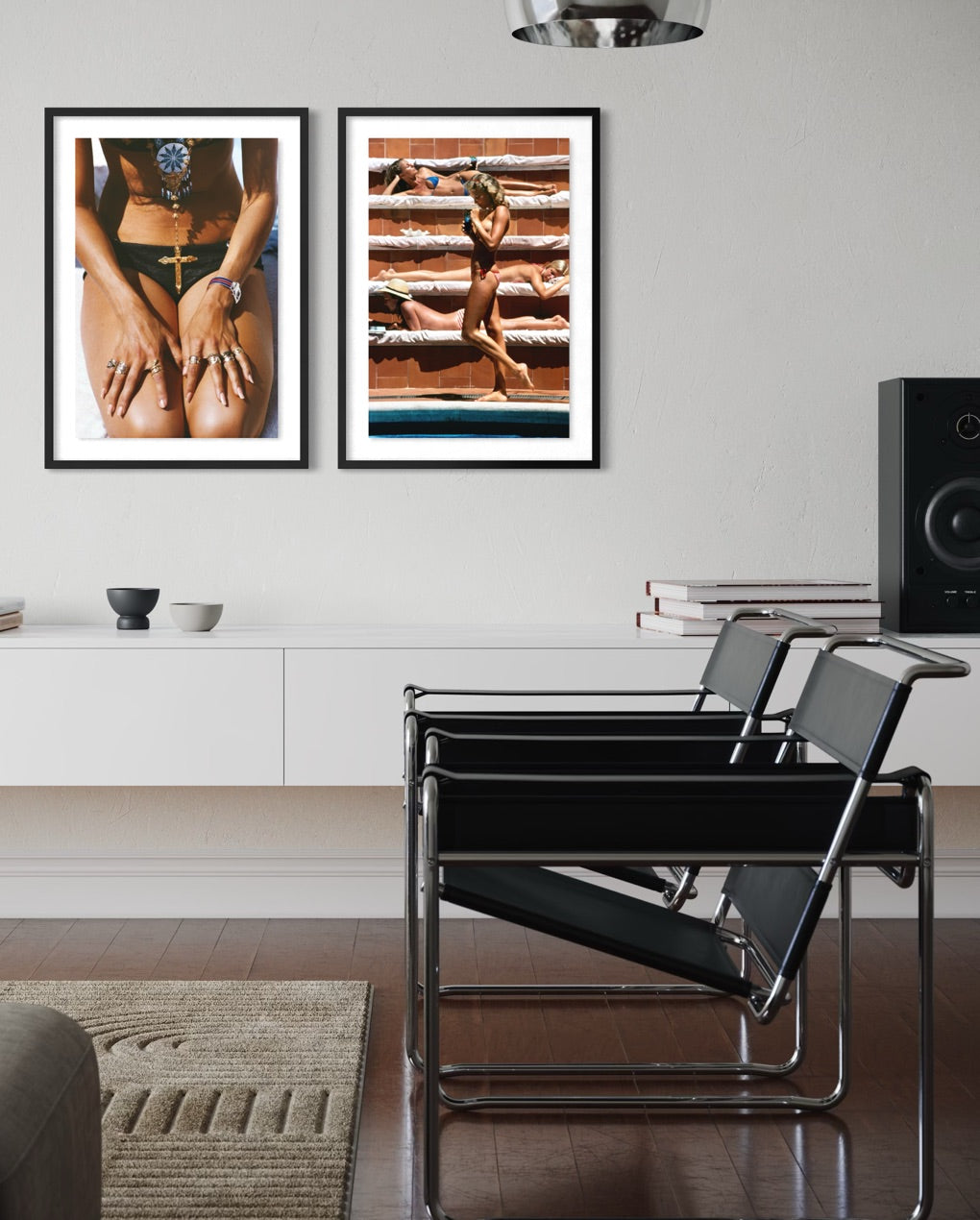 A styled interior room showing two framed art prints hanging on a white wall above a white console. The left print features a close-up of a person's torso in a green bikini, and the right print shows a woman standing on wooden steps wearing a bikini.
