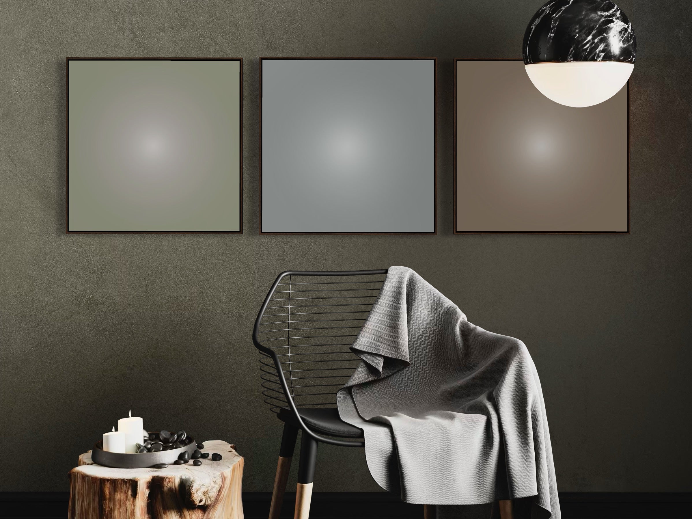 Three framed artworks on a dark wall with a chair draped with a gray blanket.