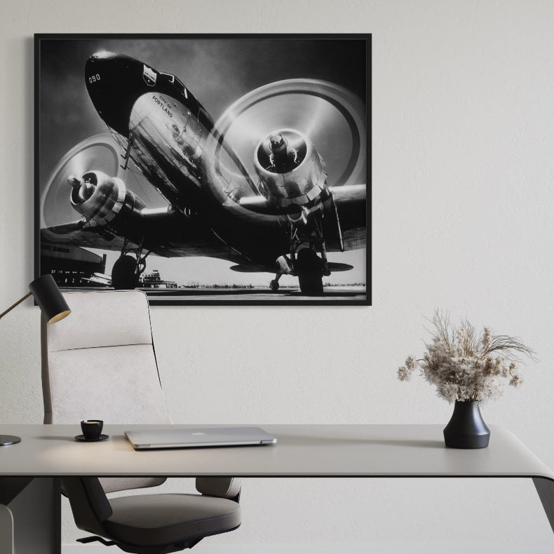 Framed black and white airplane photograph on a wall above a desk.