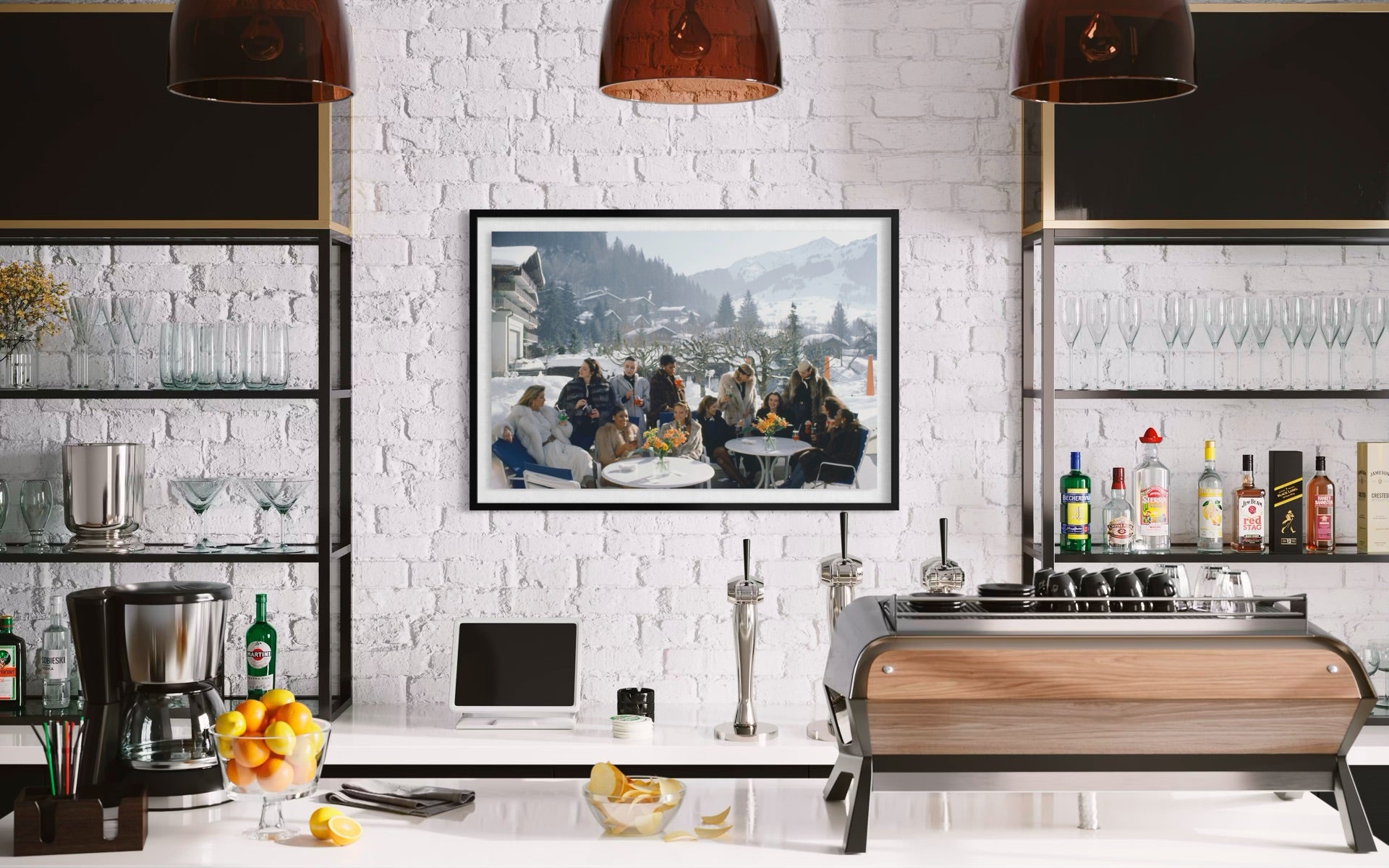 A framed art print depicting a group of people dining outdoors in a snowy mountain setting, displayed on a white brick wall above a modern kitchen counter with coffee equipment and bar shelves.
