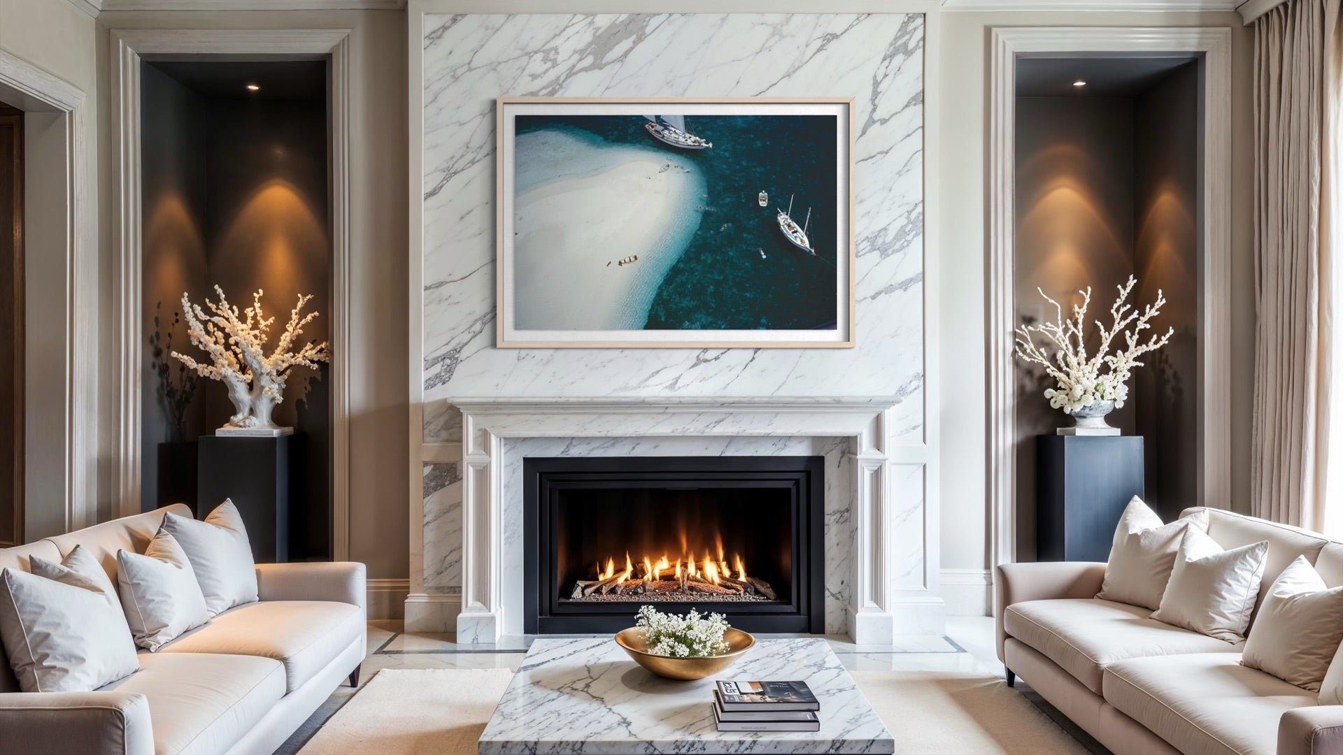 A framed abstract coastal artwork hangs above a fireplace in a modern living room with cream sofas, marble surfaces, and warm ambient lighting. The Picturalist Wall Art and Photography for Designed Interiors. 