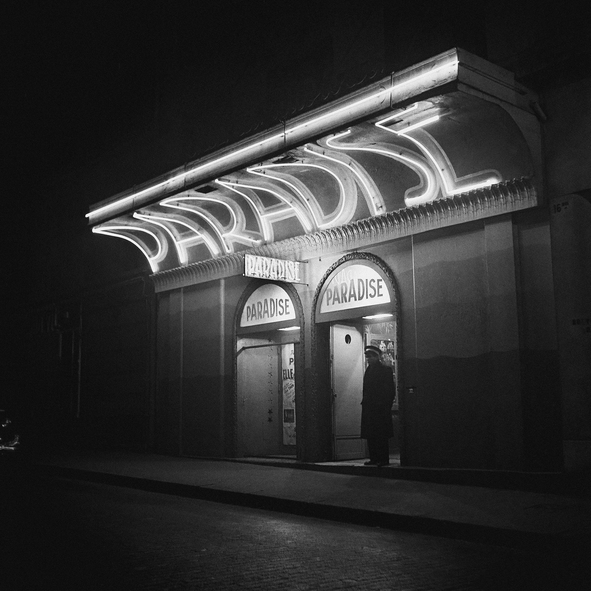 Paris at Night by Michael Ochs Archive showing the glowing Paradise cinema marquee in Paris, fine art black and white photograph framed by The Picturalist