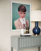 Framed portrait of audrey hepburn on a wall above a table with decorative items.