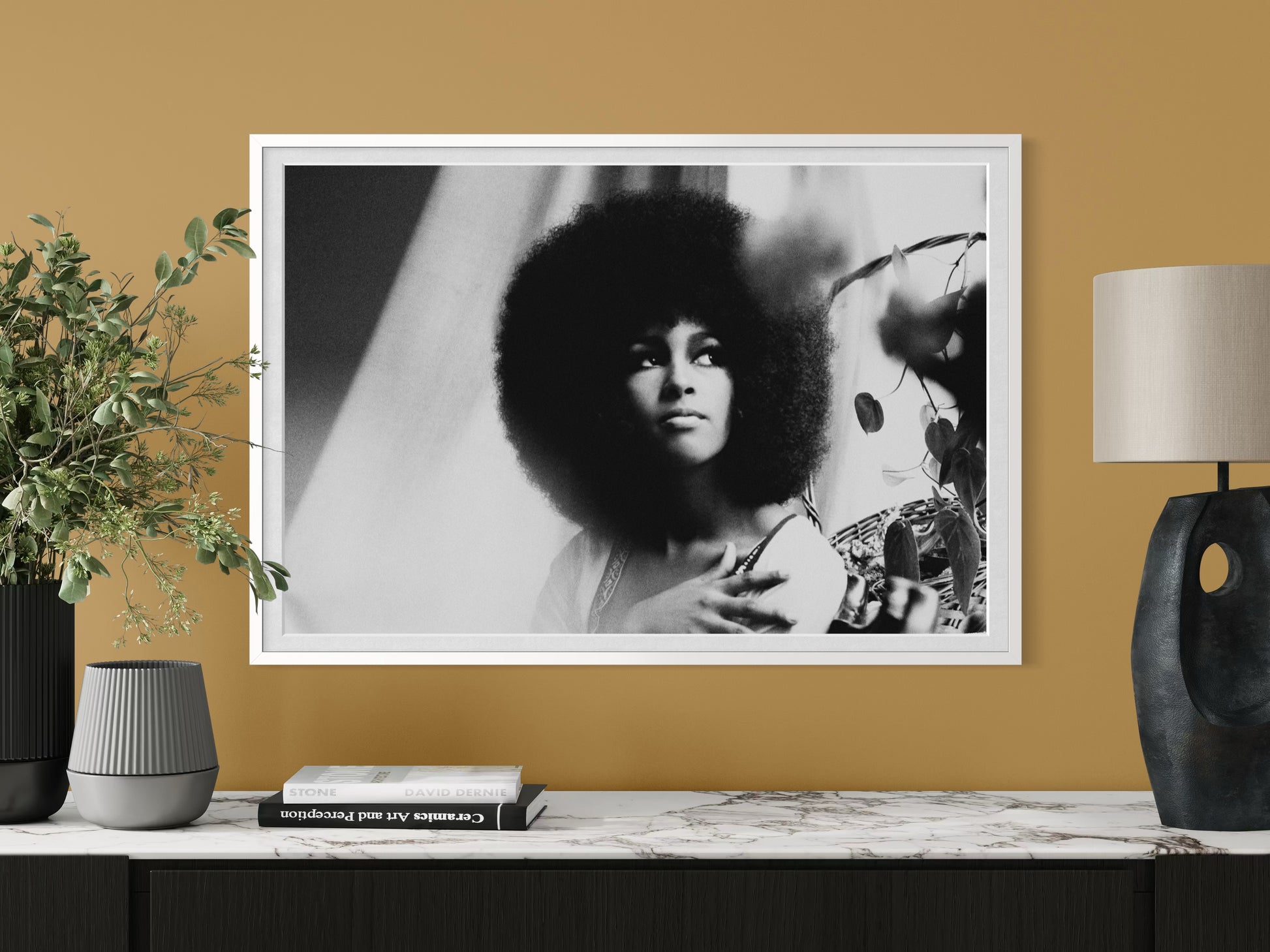 Framed black and white portrait of a woman with an afro on a wall with decor items below.