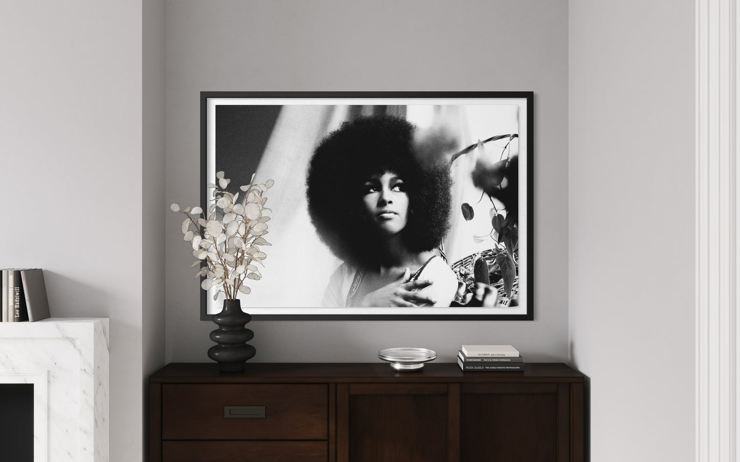 Framed black and white portrait of a person with an afro on a wall above a wooden cabinet.