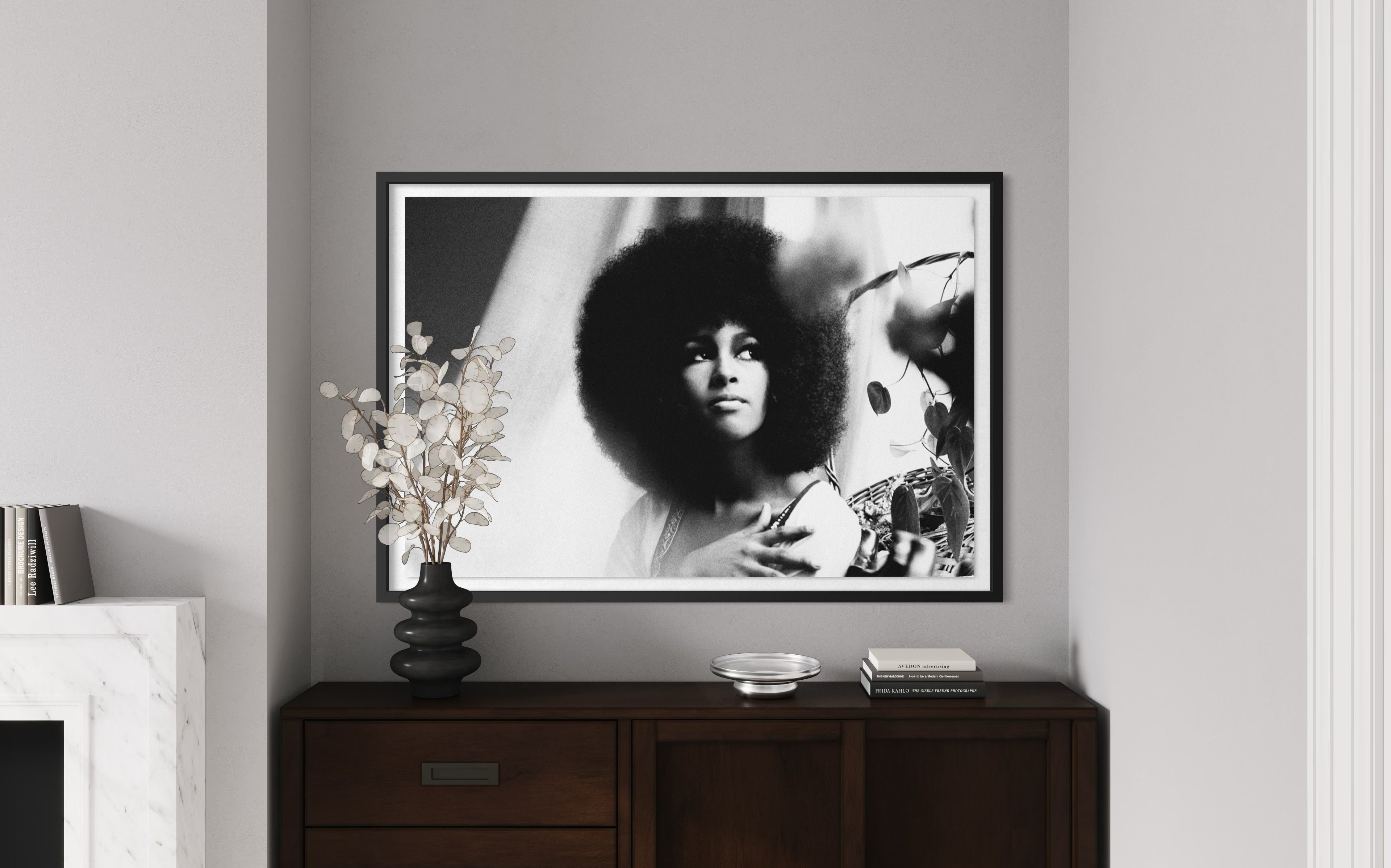Framed black and white portrait of a person with an afro on a wall above a wooden cabinet.