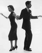 A black and white photograph of a man and a woman demonstrating a dance pose, both are dressed in vintage clothing, with the man in a suit and the woman in a sleeveless dress.