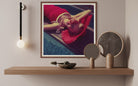 Framed artwork of a person in a red dress lying on a poolside, displayed on a wooden shelf with decorative items.