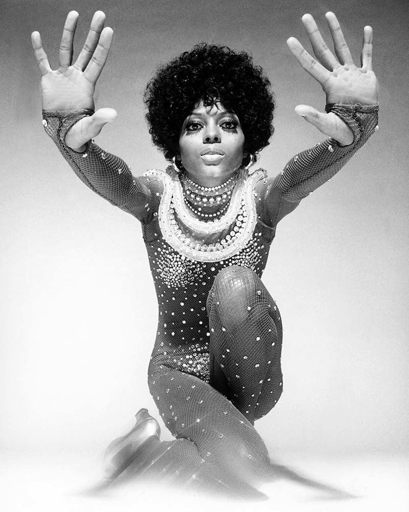 A black and white photograph of Diana Ross with her arms raised, wearing a sparkling outfit.