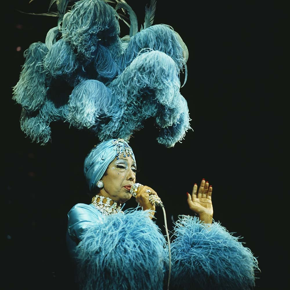 A colorful photograph of Josephine Baker in an elaborate blue costume with feathers, performing on stage.