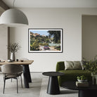 A framed landscape art print of a scenic coastal road with a purple car, displayed on a light beige wall in a modern, stylishly decorated living room.