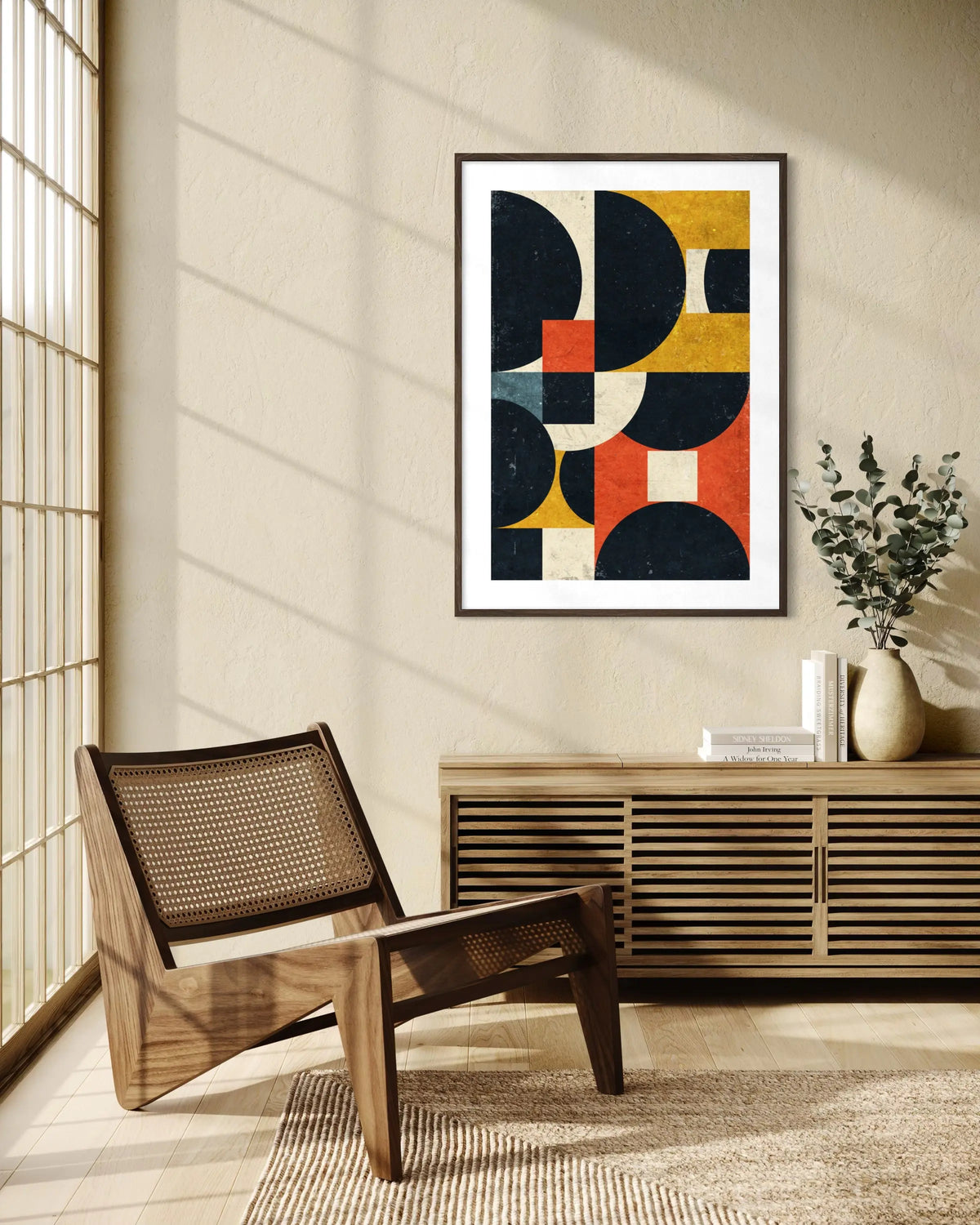 A framed abstract geometric wall art print hangs on a beige wall in a styled interior room with a wooden chair, cabinet, and vase.
