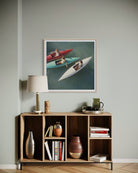 A framed art print depicting two speedboats on water, styled in a modern living room setting above a wooden bookshelf with a lamp and decorative items.
