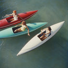 Three women sit in narrow, boat-like watercraft on open water. One craft is red, one is aqua/turquoise, and one is white, arranged diagonally across blue-green water.