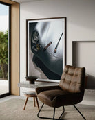 A large framed wall art print depicting a close-up of a silver car headlight and dashboard is displayed in a modern living room setting above a brown leather armchair.