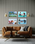 A set of four framed tropical beach and poolside art prints displayed on a gray wood-paneled wall above a brown leather sofa in a modern living room setting.