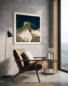 A framed art print of a volcanic landscape hangs on a textured gray wall in a modern living room setting with a brown leather armchair, a black floor lamp, and a side table.