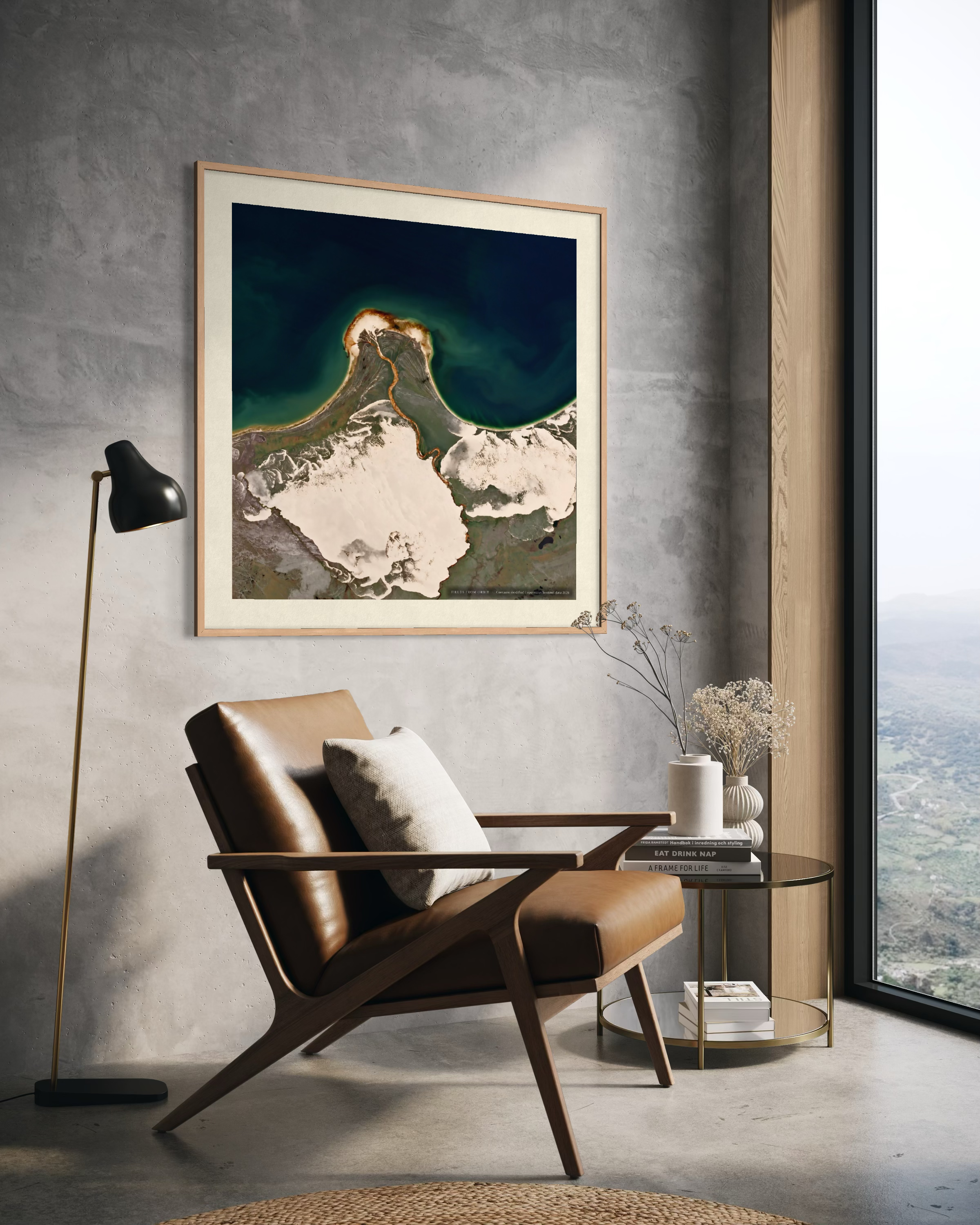 A framed art print of a volcanic landscape hangs on a textured gray wall in a modern living room setting with a brown leather armchair, a black floor lamp, and a side table.