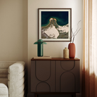 A framed art print of a snowy mountain peak under a dark teal sky, styled on a dark wood sideboard in a modern living room setting.