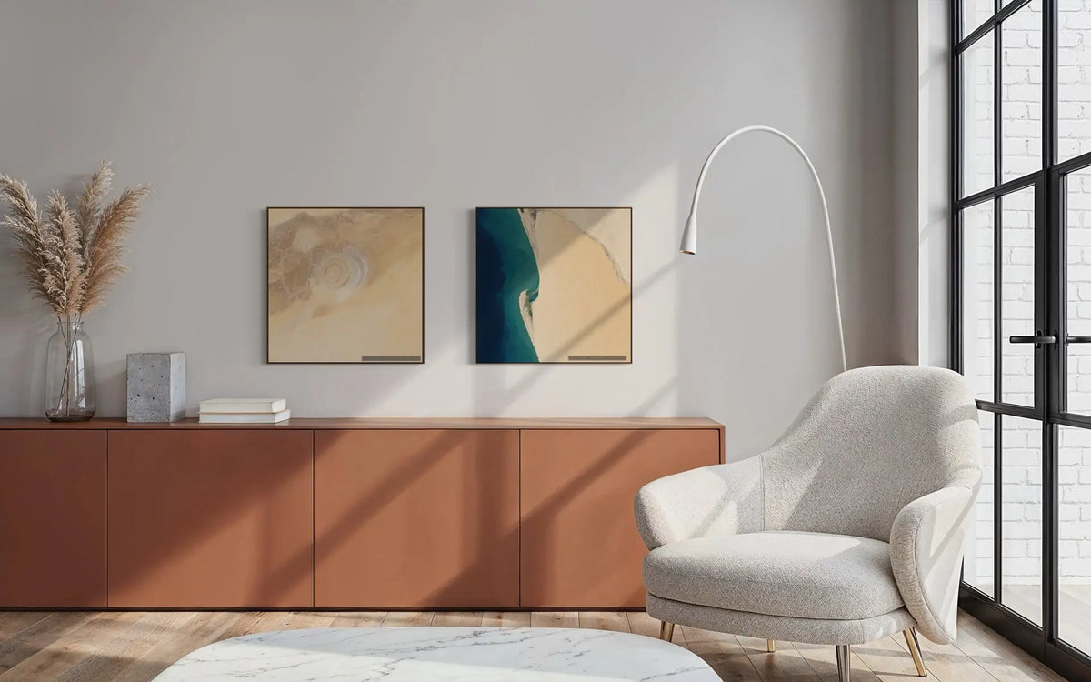 A styled interior room scene with two framed abstract wall art prints hanging above a terracotta sideboard. The right print features a bold vertical teal and beige design, while the left print is a softer beige and cream swirl.