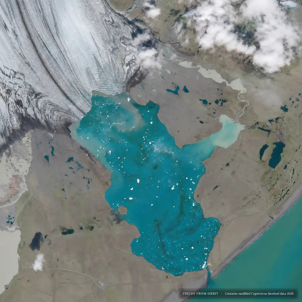 Paul Laffin The Iceberg Lagoon No. 1, satellite artwork of turquoise Jökulsárlón and white icebergs in Iceland.Satellite view of a glacial lake with bright turquoise water, surrounded by tan and brown land, clouds, and a large glacier or ice field. Small text at the bottom reads 'FIELDS FROM ORBIT - Contains modified LERSATized satellite data 2024'.