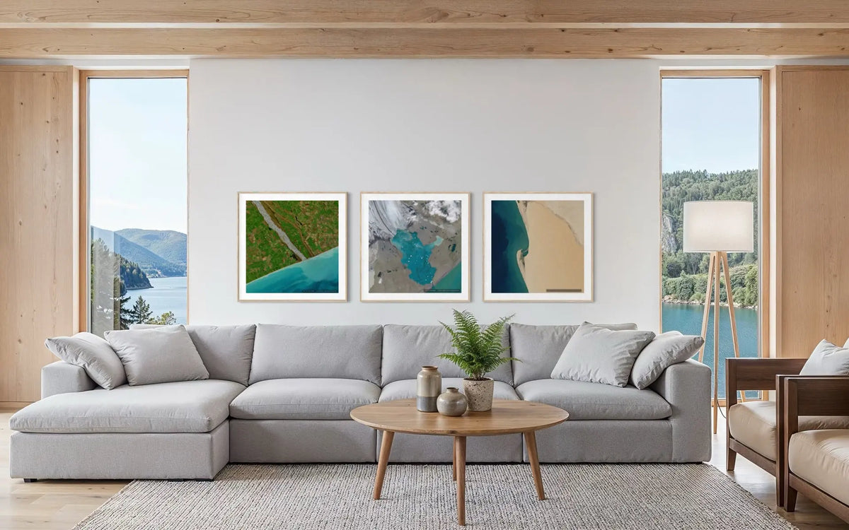 Three framed abstract landscape art prints with teal, green, and beige tones are displayed in a row on a white wall above a modern light gray sectional sofa in a bright, contemporary living room.