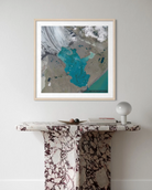 A framed art print featuring a modern abstract map of Iran in teal, gray, and white, styled on a light gray wall above a marble console table with a white lamp.