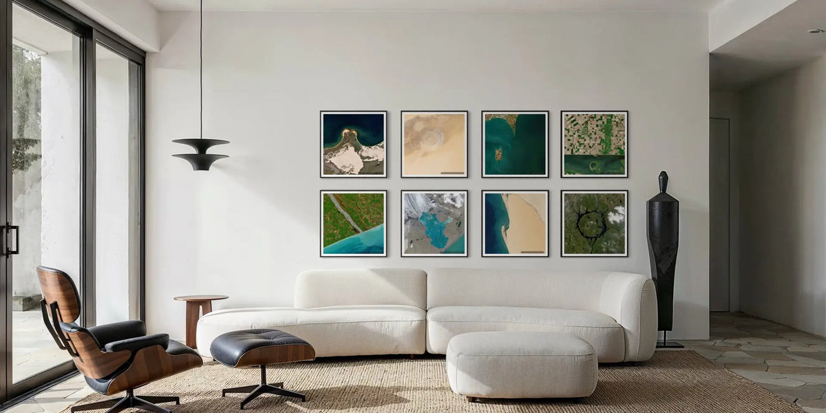 A modern living room with a white sectional sofa, matching ottoman, black lounge chair, and a wall grid of eight framed abstract art prints in earthy teal, beige, and green tones.