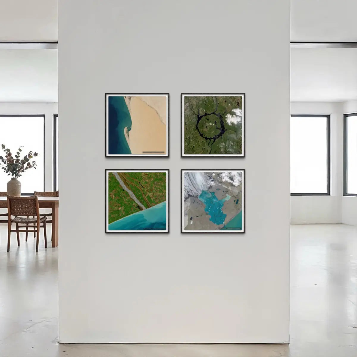 Four framed abstract landscape art prints arranged in a 2x2 grid on a white wall in a modern, minimalist room with large windows and a dining area visible in the background.