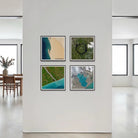 Four framed abstract landscape art prints arranged in a 2x2 grid on a white wall in a modern, minimalist room with large windows and a dining area visible in the background.