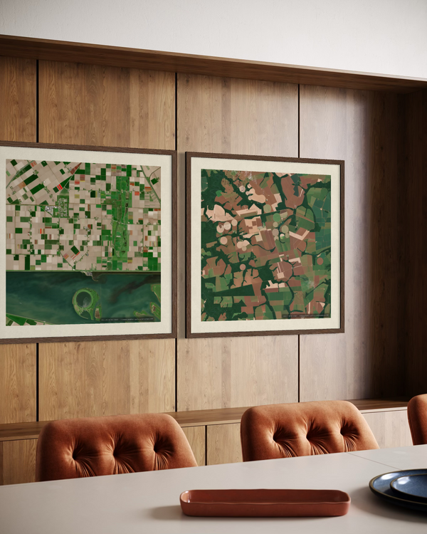 Two framed abstract landscape art prints with green and brown tones hang on a wood-paneled wall above a dining table with tufted brown chairs.