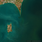 Satellite view of a coastal landscape with a small peninsula on the left, a large body of deep blue-green water on the right, and a narrow strip of shoreline at the top edge.