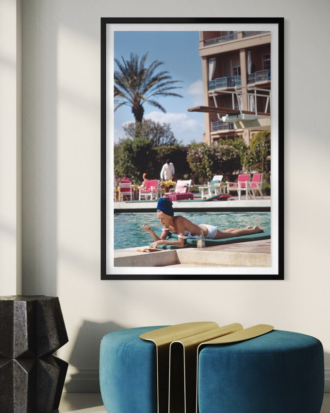 Framed photograph of a woman by a pool with palm trees and a building in the background, displayed on a wall.