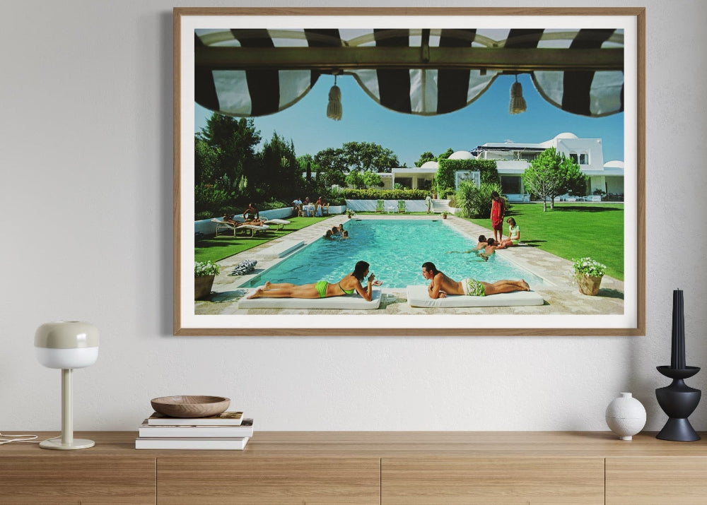 Framed artwork of a pool scene on a wall above a wooden cabinet.