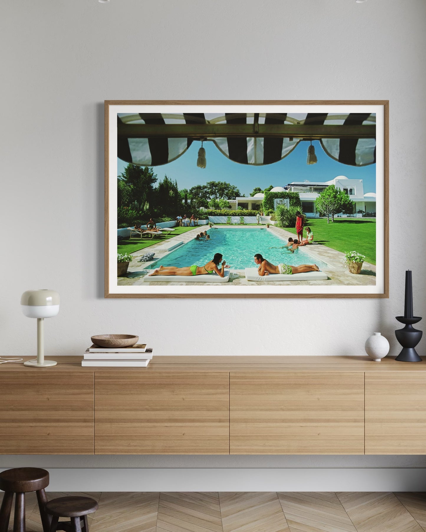 Framed artwork of a pool scene on a wall above a wooden cabinet.