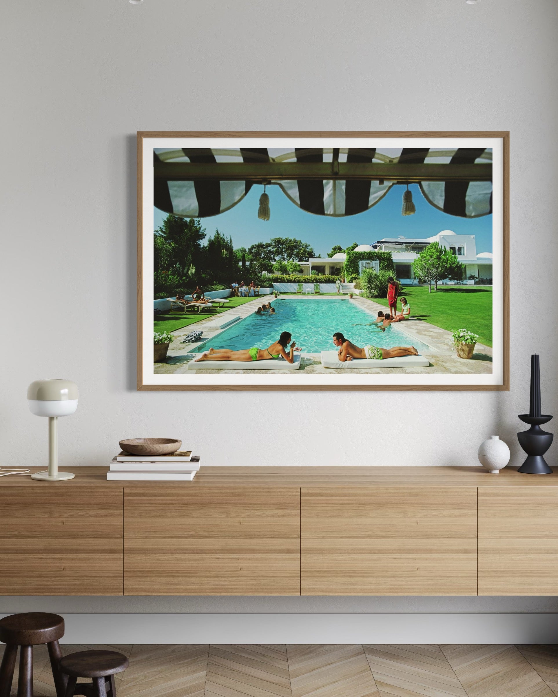 Framed artwork of a pool scene on a wall above a wooden cabinet.